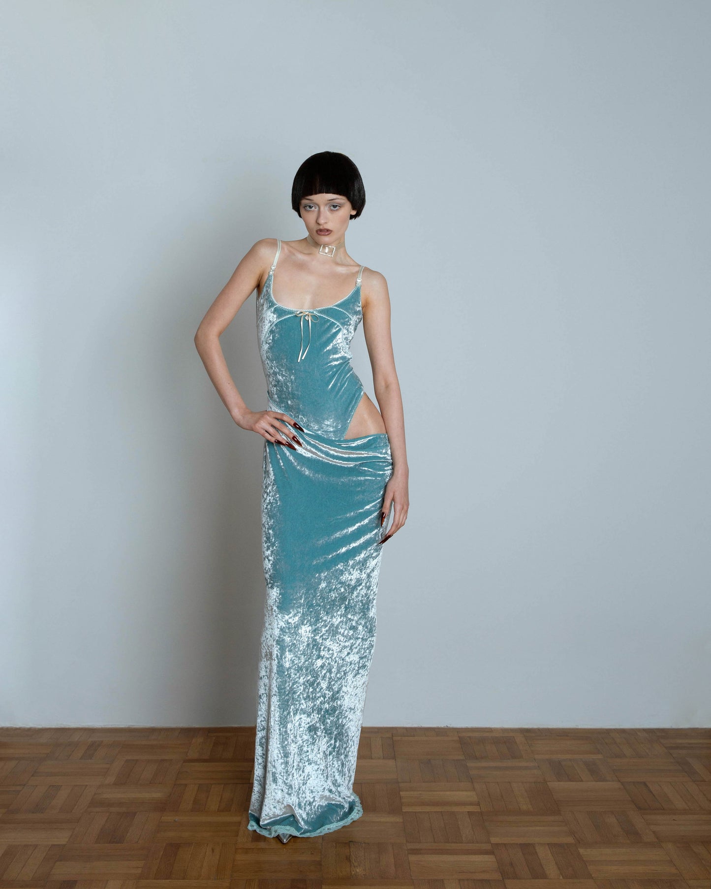 A model wearing a mint green maxi dress with an open hip and spaghetti straps. The dress features a fitted bodice and a flowing skirt with lace detailing at the hem.