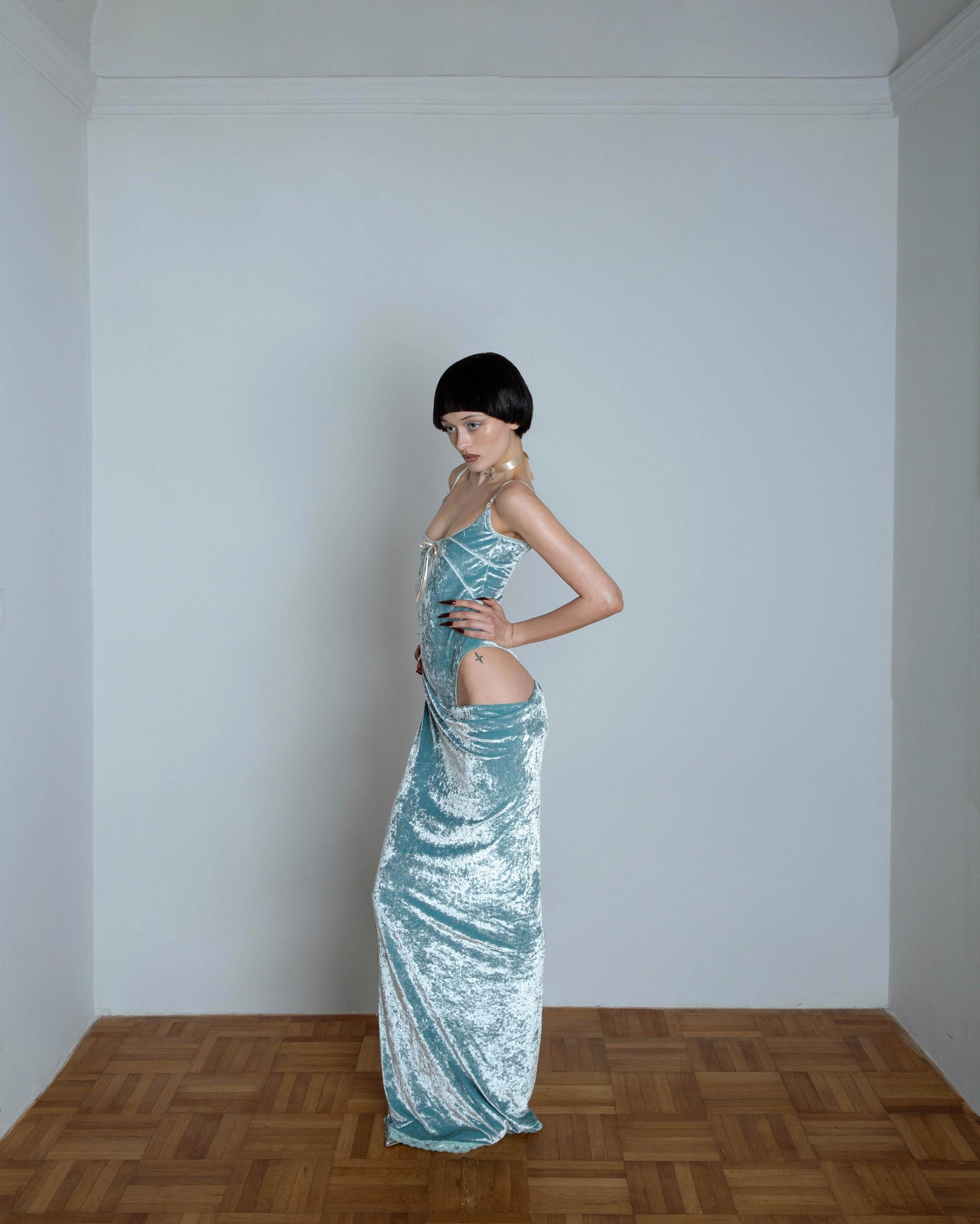 A model wearing a mint green maxi dress with an open hip and spaghetti straps. The dress features a fitted bodice and a flowing skirt with lace detailing at the hem.