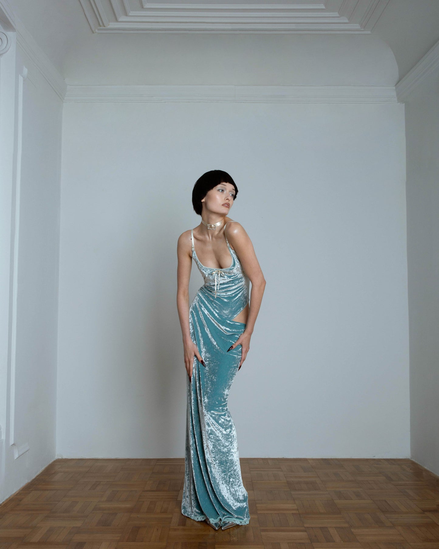 A model wearing a mint green maxi dress with an open hip and spaghetti straps. The dress features a fitted bodice and a flowing skirt with lace detailing at the hem.