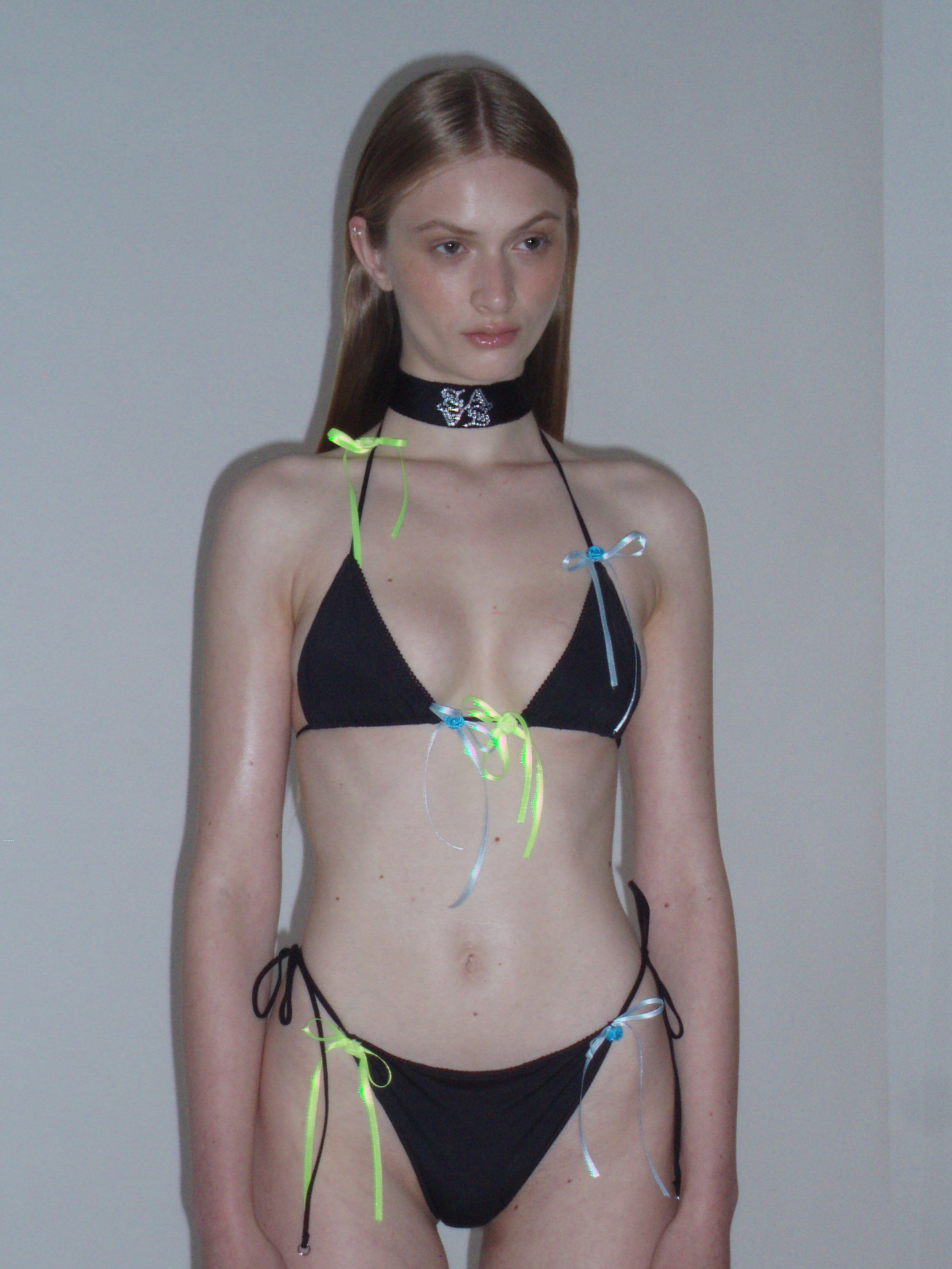 Model wearing a black bikini with colorful strings against a plain background
