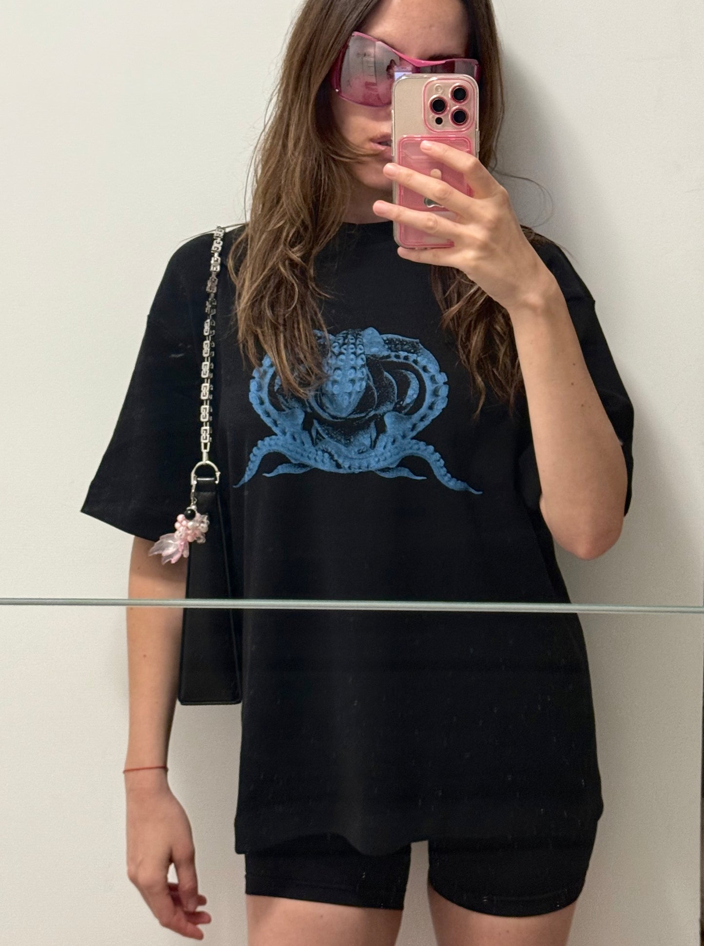 Person wearing a black t-shirt with a blue graphic design, taking a mirror selfie.