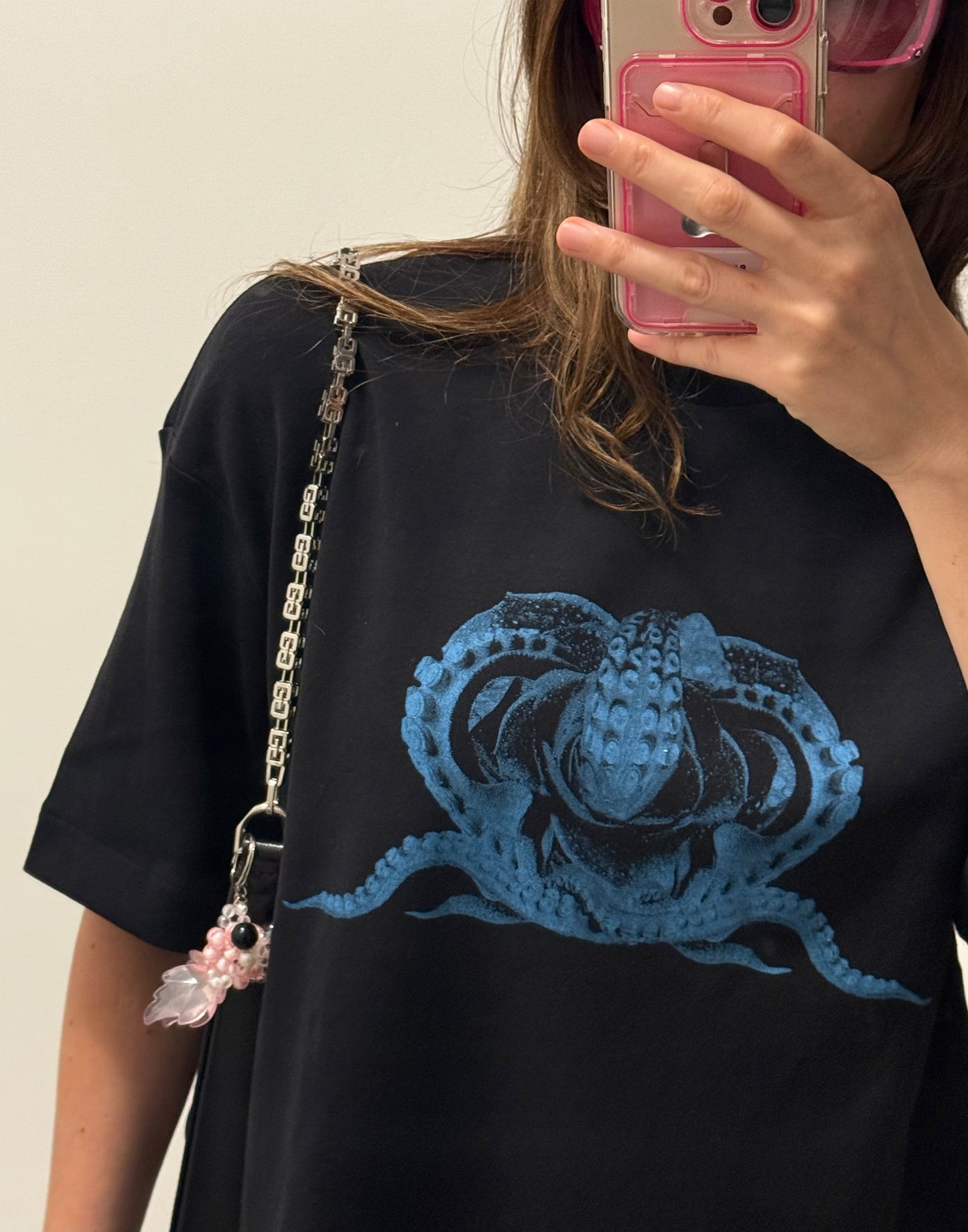 Person wearing a black t-shirt with a blue graphic design, holding a phone with a pink case.