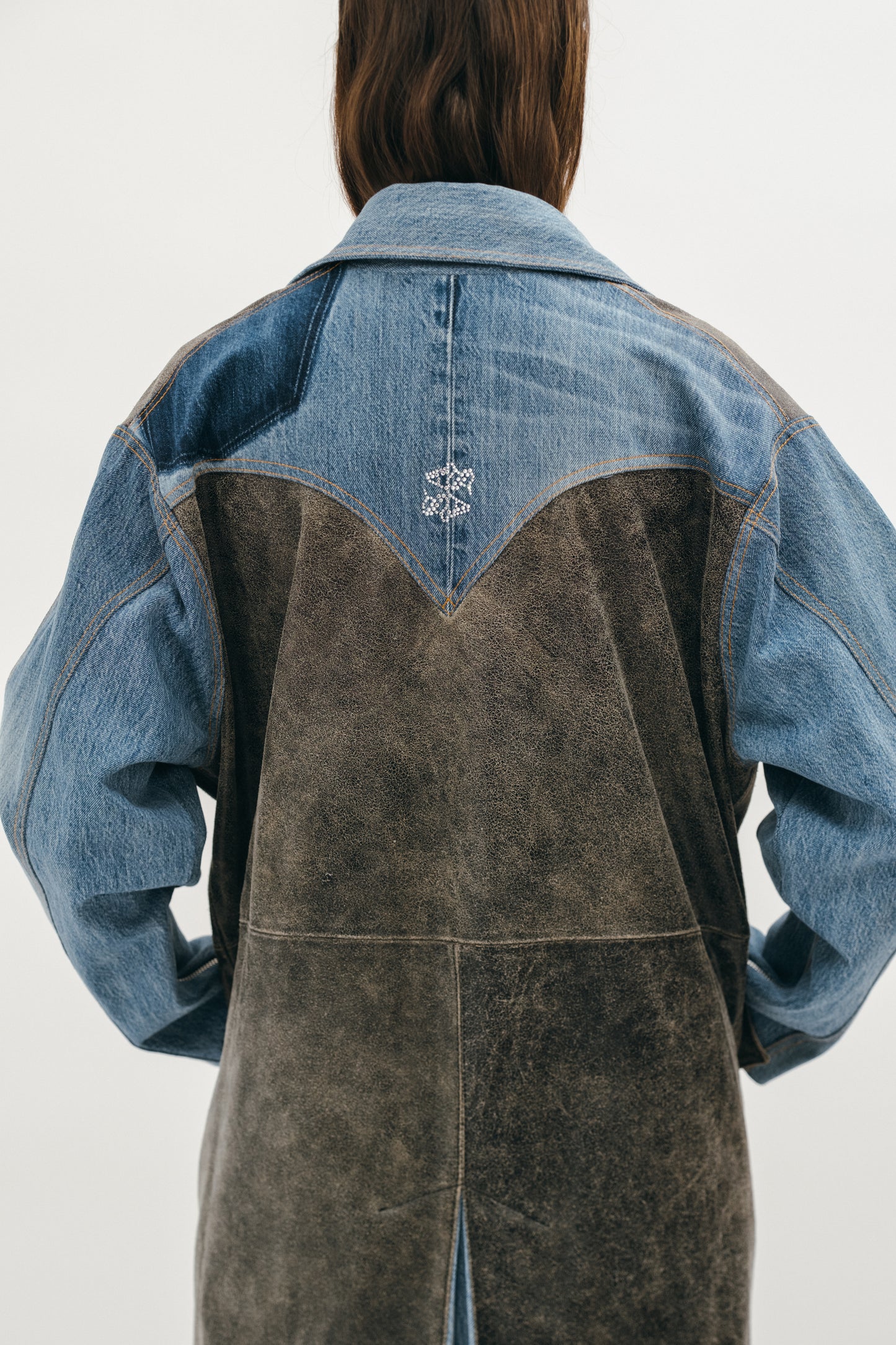 A woman wearing a coat made of denim and leather showing the back of the coat focusing on the rhino logo