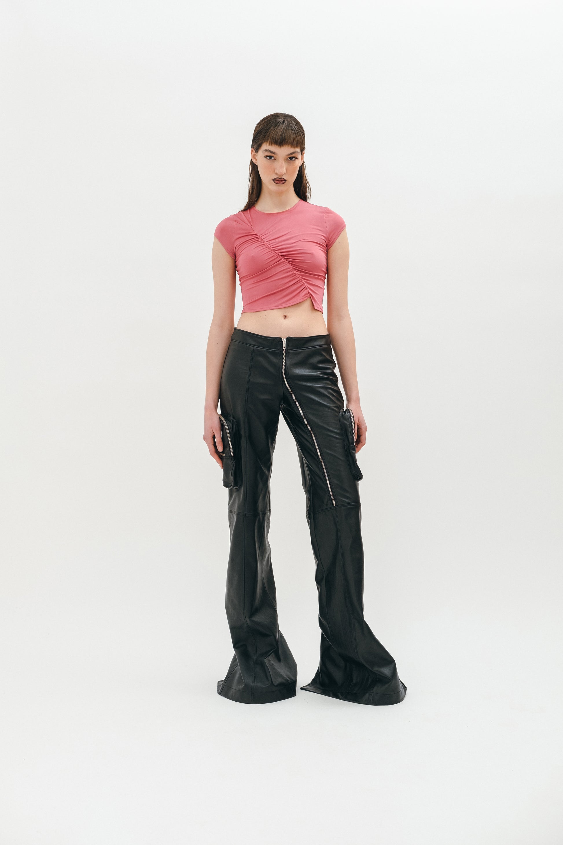 A person standing wearing black leather pants with cargo pockets, zip slits on the back, and a pink top.